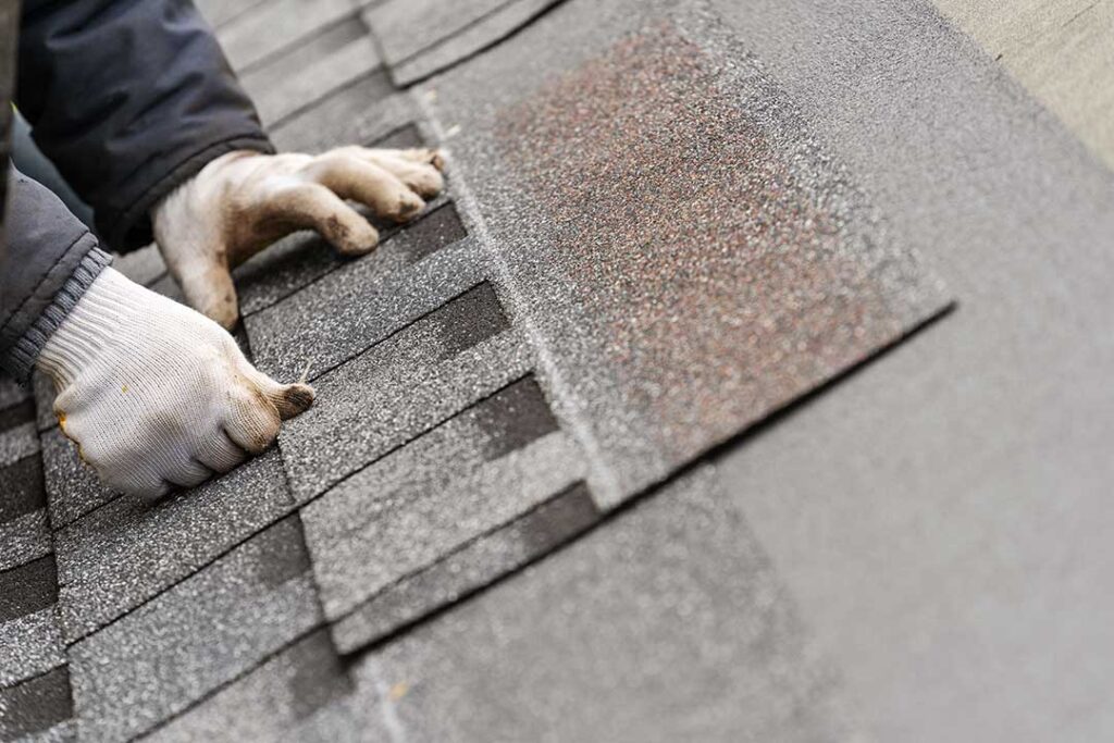 Homeowner inspecting gutters and roof edges beside a snow-ready house in autumn.